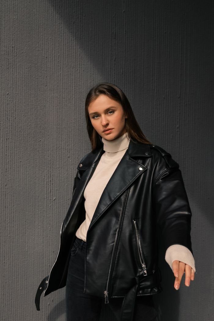 Home Young woman posing confidently in a black leather jacket and turtleneck sweater.